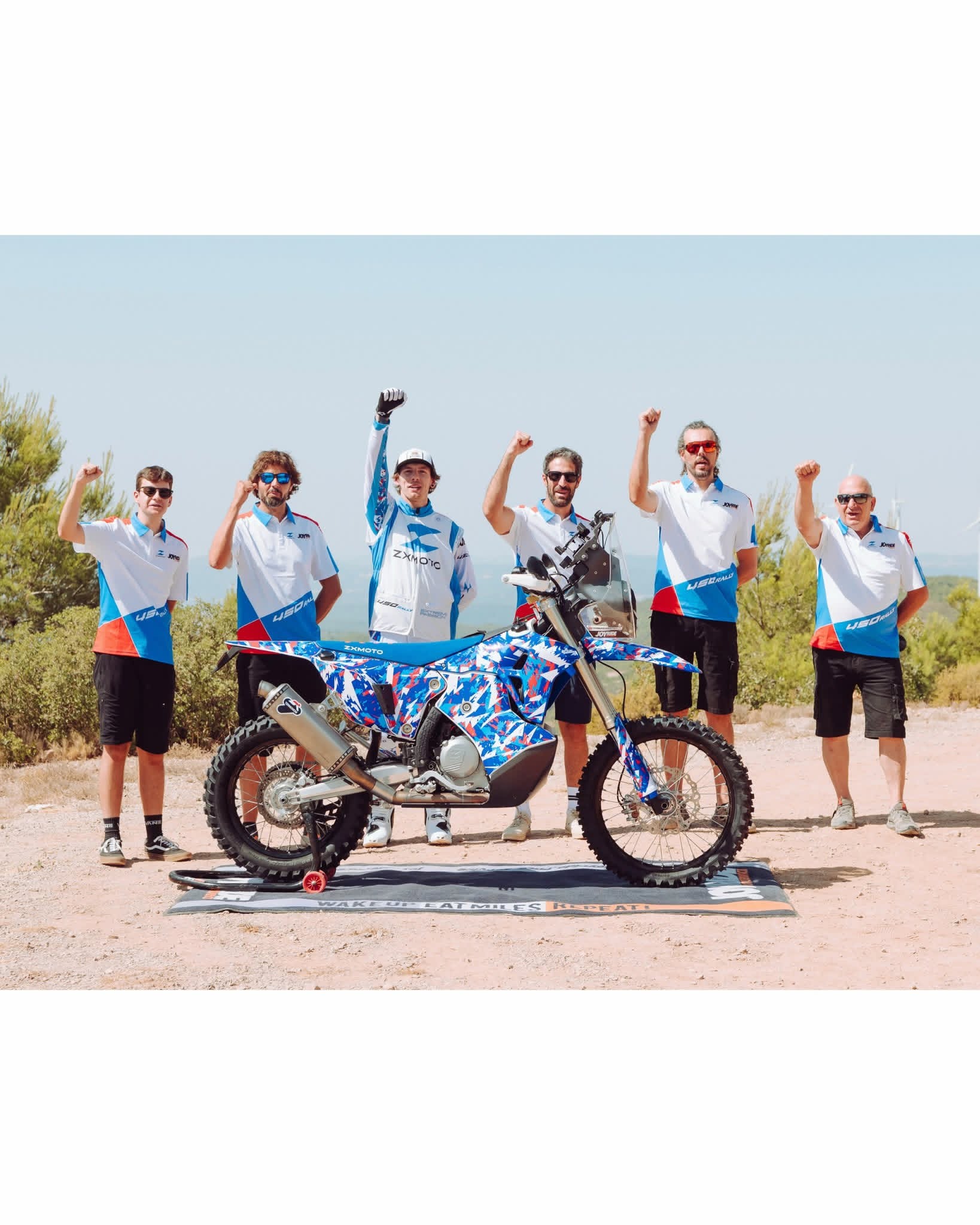 Đội ZXMOTO giơ tay chào bên chiếc xe rally 450 sơn họa tiết xanh đỏ